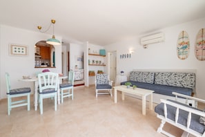 A living room with a sofa, chairs, a table, and a kitchen in the background.