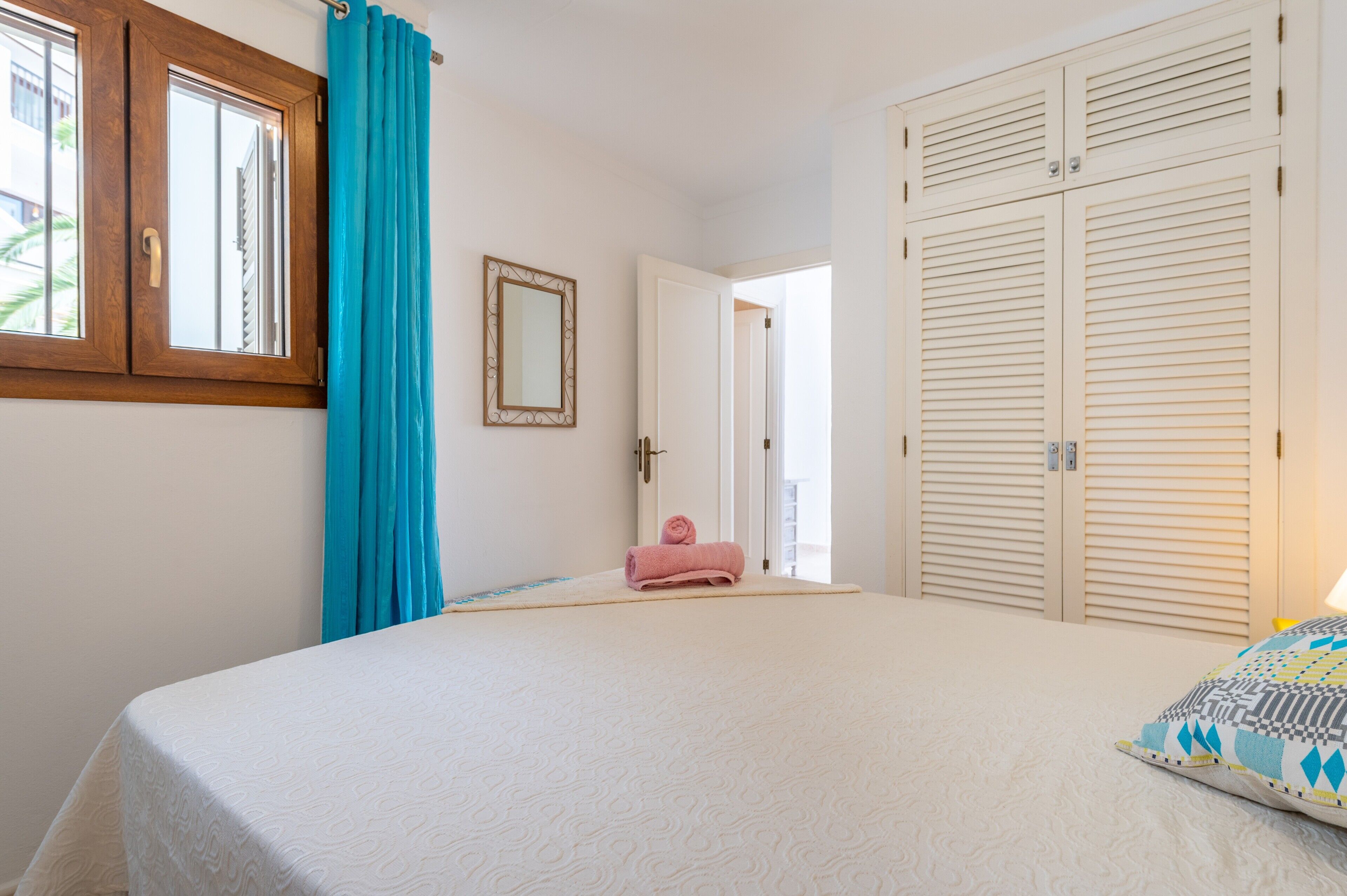 A bedroom with a bed, a window with curtains, a door, and a wardrobe.