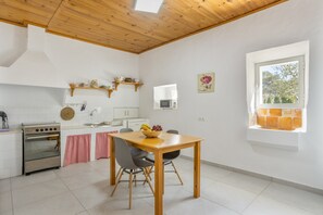 A kitchen with a wooden ceiling, white walls, a stove, and a dining table with chairs.