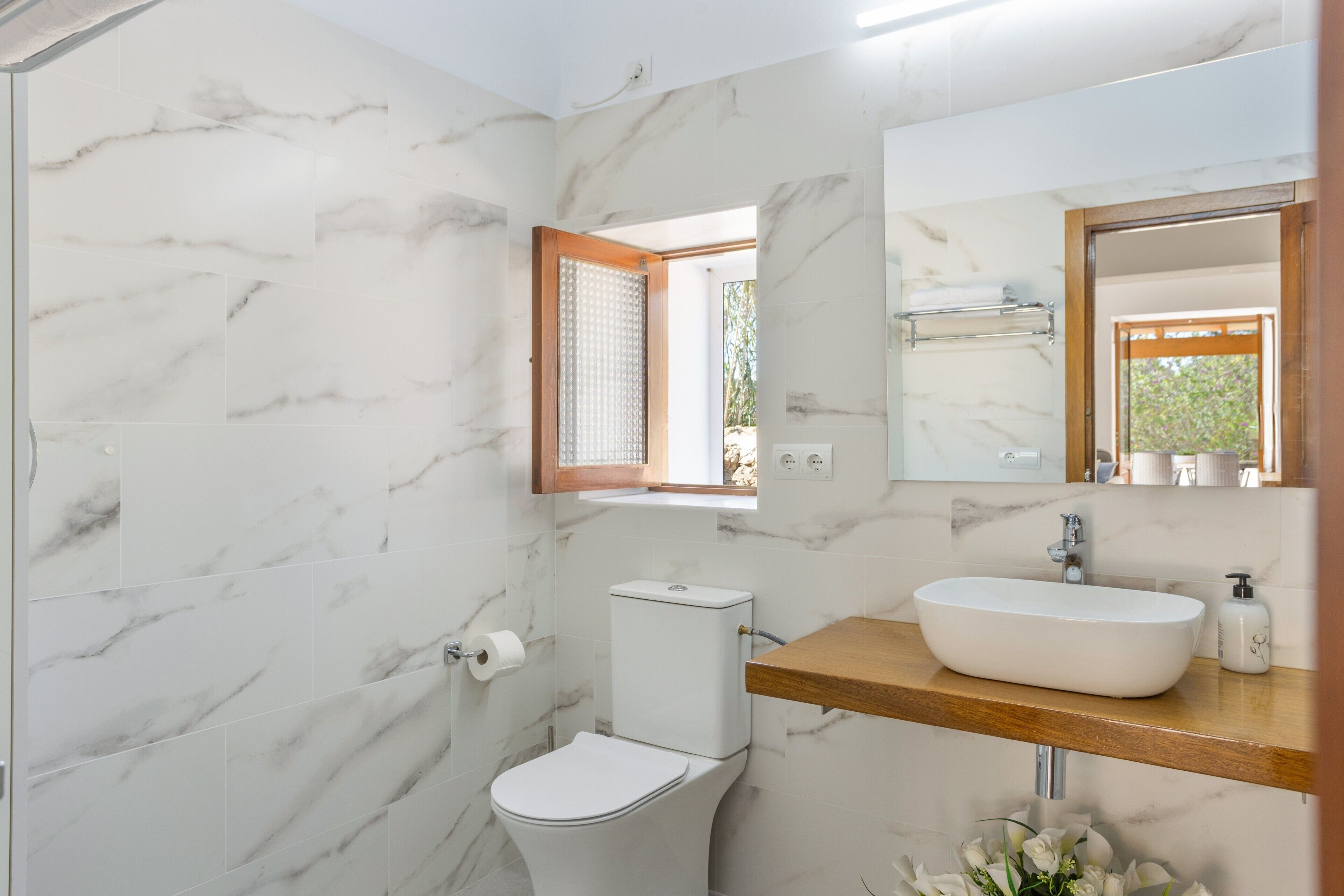 Une salle de bain équipée de toilettes, d’un lavabo, d’un miroir et d’une fenêtre avec un cadre en bois.