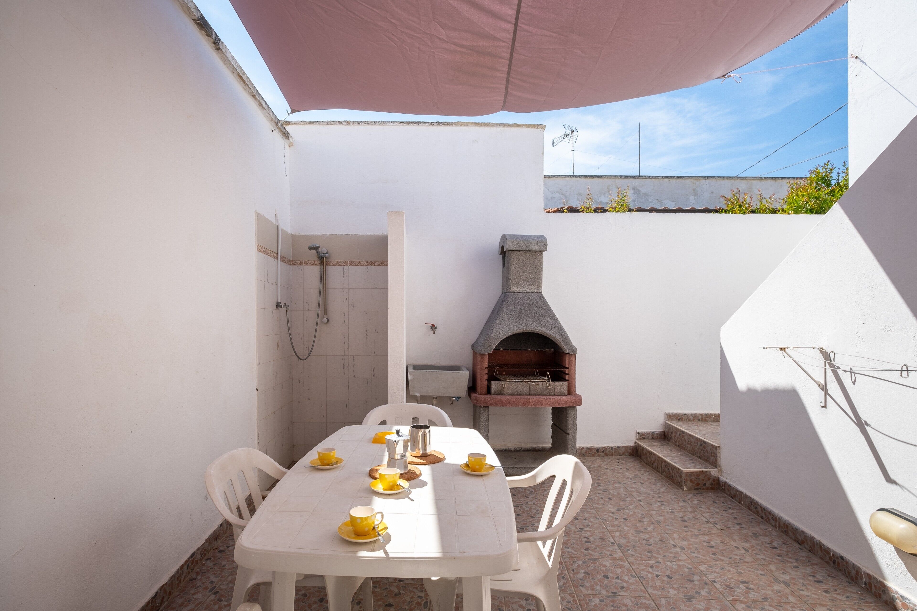 Un patio con una mesa preparada para cuatro personas, un horno de piedra y un área de ducha.