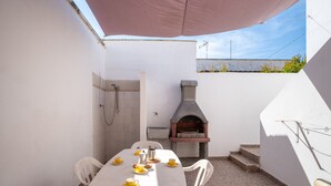 Une terrasse avec une table dressée pour quatre personnes, un four en pierre et un espace douche.