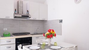 Une cuisine moderne avec des meubles blancs, un four encastré et un coin repas agrémenté d’une table blanche mise pour deux personnes.