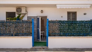 Un bâtiment blanc avec une porte bleue, des unités de climatisation et un petit hall d’entrée.
