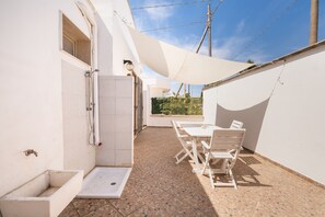 Een terras met een tafel, stoelen, een douche en een witte muur.