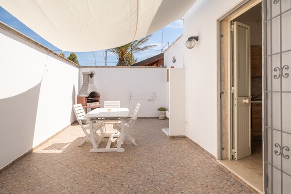 Een terras met een tafel, stoelen, een barbecue en een deur naar een keuken.