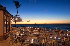 Enjoy ocean views from this outdoor dining area, featuring wicker tables and chairs under twinkling string lights.