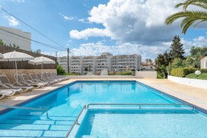 A swimming pool with lounge chairs, a building in the background, and a clear sky.