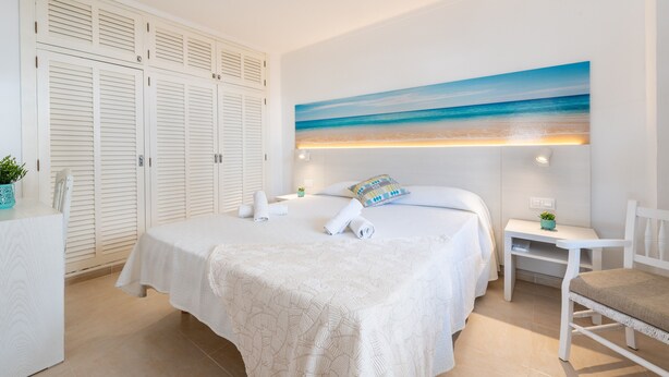 A bedroom with a bed, a nightstand, a chair, a wardrobe, and a painting of a beach. - "Erizo De Mar" with Sea Views, Wi-Fi, and Air Conditioning (Tourist Tax Included) (Felanitx)