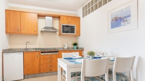 A compact kitchen with wooden cabinets, a built-in microwave, and a dining area with chairs and a table set for two. - "Erizo De Mar" with Sea Views, Wi-Fi, and Air Conditioning (Tourist Tax Included) (Felanitx)