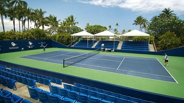 A tennis court with blue seating and white canopies, surrounded by palm trees. - Waikoloa | Pool & Beach Access | 2BR Premier - 2BX (Waikoloa Village)