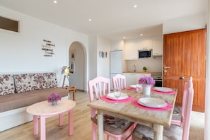 A dining area with pink chairs, a wooden table, and a sofa with patterned cushions.