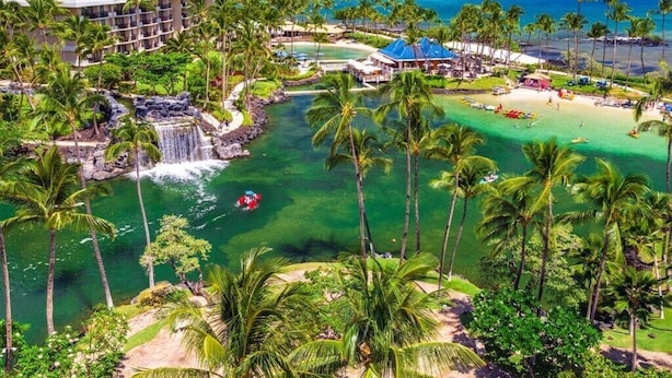 Een resort met zwembad, palmbomen, waterval en strand.