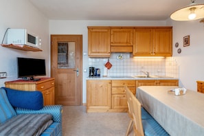 A compact kitchen with wooden cabinets, a microwave, a sink, and a dining area with a table and chairs. - Apartment 'Malsötscherhof A' with Mountain View, Private Terrace and Wi-Fi (Villanders)
