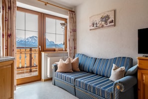 A room with a sofa, a window with curtains, a radiator, and a painting on the wall.