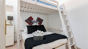Quarto com beliche, mesa de cabeceira, televisão fixada na parede e dois objetos decorativos na parede.