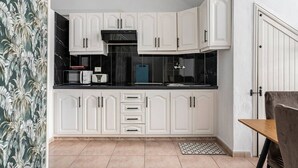 Cozinha compacta com armários brancos, bancada preta e micro-ondas.