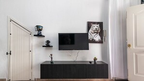 Quarto com televisão fixada na parede, um armário escuro abaixo e uma porta branca à esquerda.