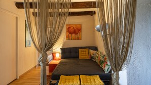 Een slaapkamer met een bed, gordijnen, een schilderij en een nachtkastje.