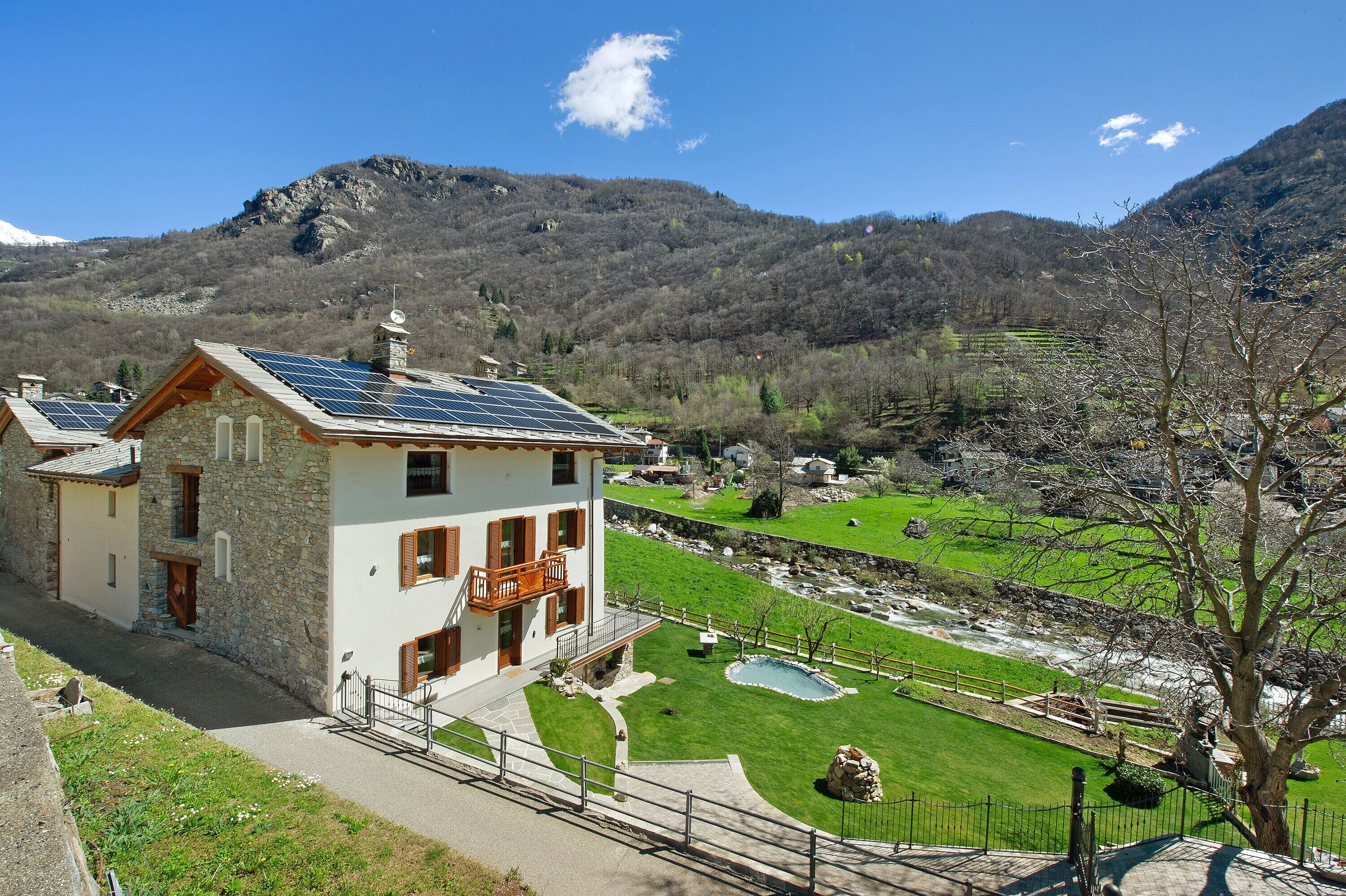 Una casa in pietra con un balcone, pannelli solari, una piscina e vista sulla valle.