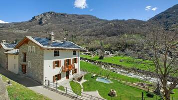 Una casa in pietra con un balcone, pannelli solari, una piscina e vista sulla valle.