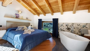 Une chambre à coucher avec un lit, une baignoire, des poutres en bois au plafond, une fenêtre avec des rideaux et une table de chevet avec une lampe.