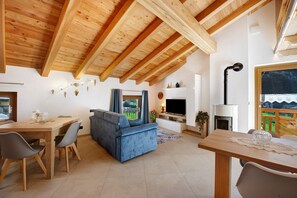 Una sala de estar moderna con techo de madera, un sofá azul, una mesa de comedor y un televisor.