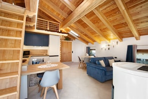 Un interior moderno con cocina, comedor y sala de estar, con vigas de madera y un sofá azul.
