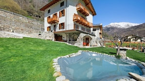 Un bâtiment à deux étages doté de balcons, d’un escalier en pierre, d’une piscine et surplombant un paysage montagneux.