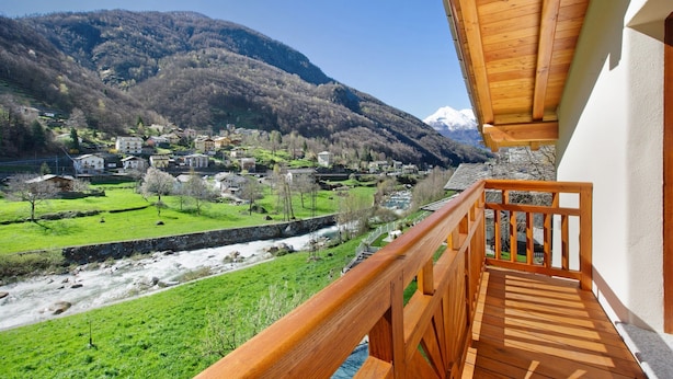 Un balcon doté d’une balustrade en bois, donnant sur une vallée où se trouvent des maisons et une rivière.