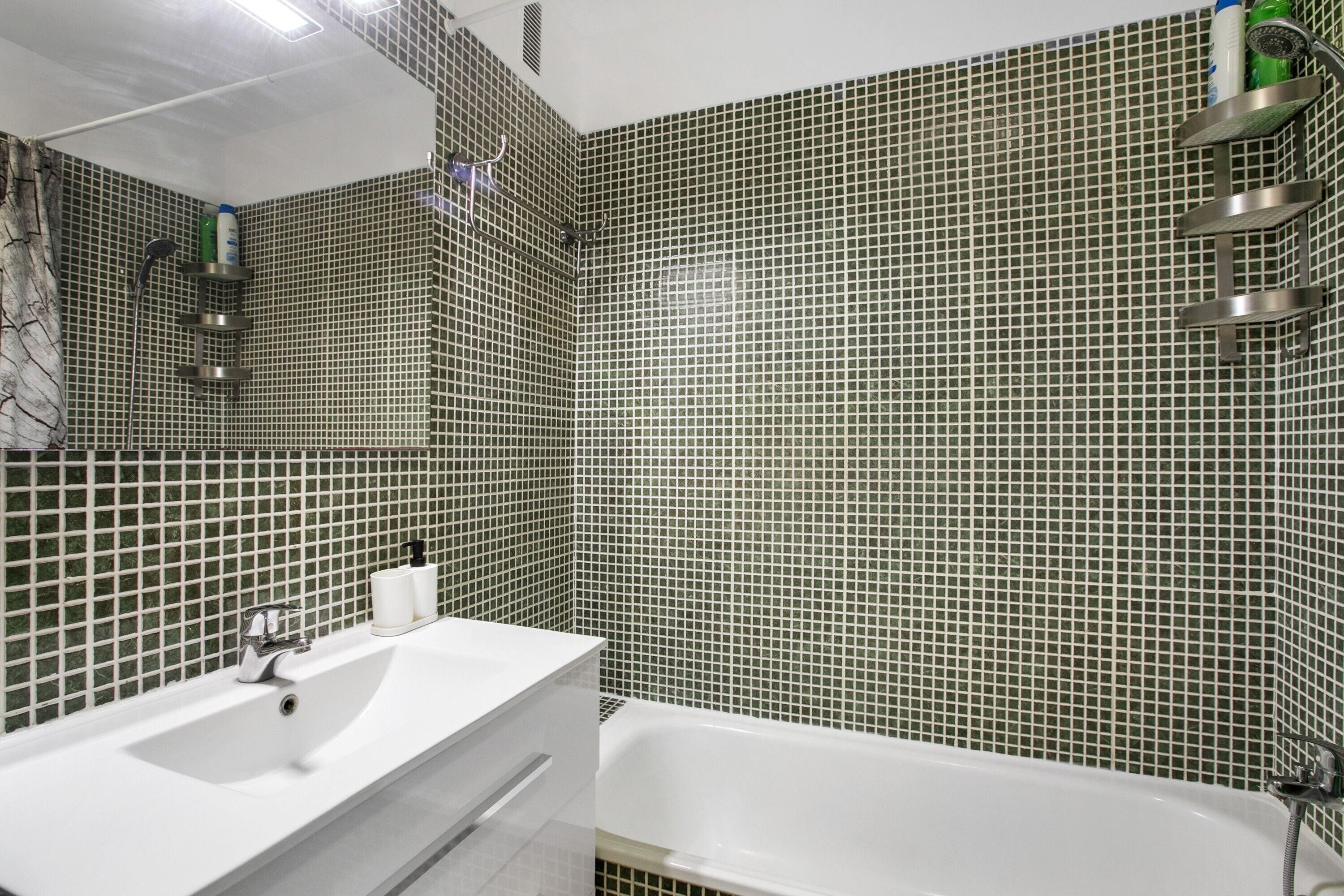 Een badkamer met een witte wastafel, een bad en een douche met een handdouche.