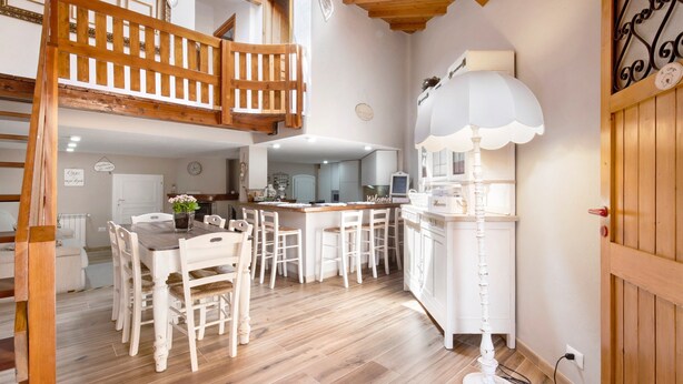 Un coin repas avec une table et des chaises en bois, une cuisine avec des meubles blancs et un lampadaire blanc.