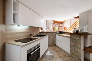 Une cuisine moderne avec des meubles blancs, une cuisinière encastrée et un pare-feu en pierre.