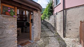 Ein Steinhaus mit einer Holztür, einer kleinen Veranda mit einer Bank und einer Steintreppe, die nach oben führt.