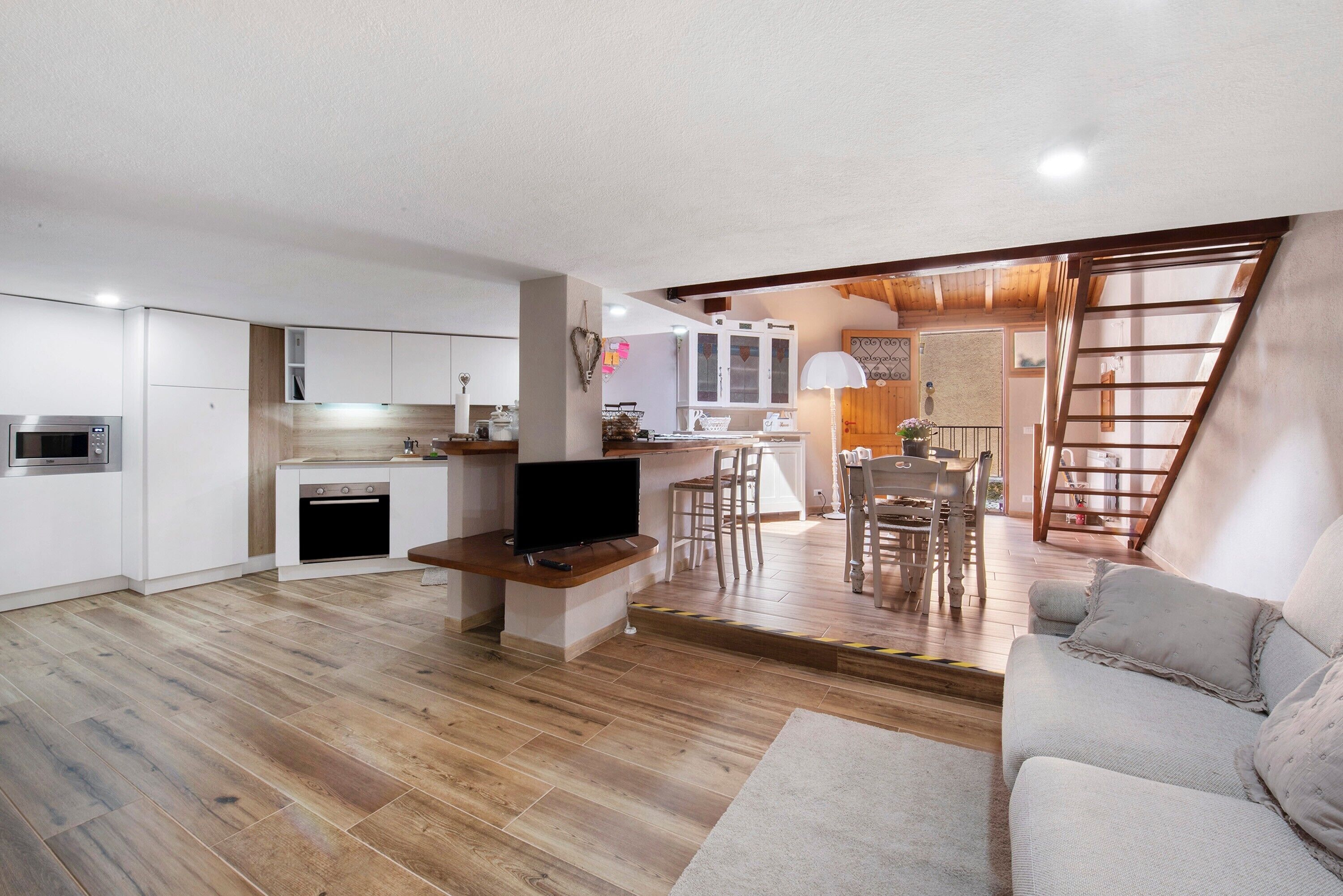 A modern kitchen with white cabinets, a built-in oven, and a TV on a wooden stand.