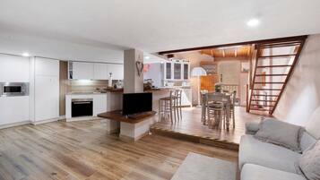 A modern kitchen with white cabinets, a built-in oven, and a TV on a wooden stand.