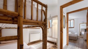 Une chambre avec un lit superposé, une table de chevet, une lampe, un miroir et une salle de bain équipée d’un porte-serviettes.