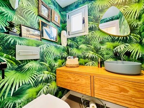 Un baño con tocador de madera, un lavamanos blanco y un espejo.