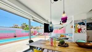 A modern interior with a pool view, a dining area with chairs and a table, and a colorful artwork on the wall. - Vacation Home "Casa Color" with Sea View, Private Pool & Wi-Fi (Corralejo)