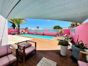 Zona de piscina con deck de madera, sillones de descanso y plantas en macetas.