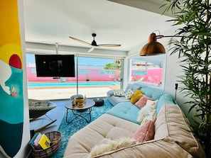 Una sala de estar con un sofá, televisor, ventilador de techo y vista a una piscina.
