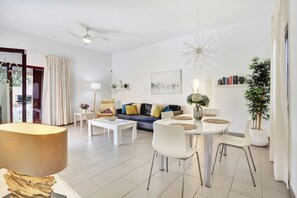 A modern living room with a sofa, coffee table, dining table, chairs, ceiling fan, and a potted plant.