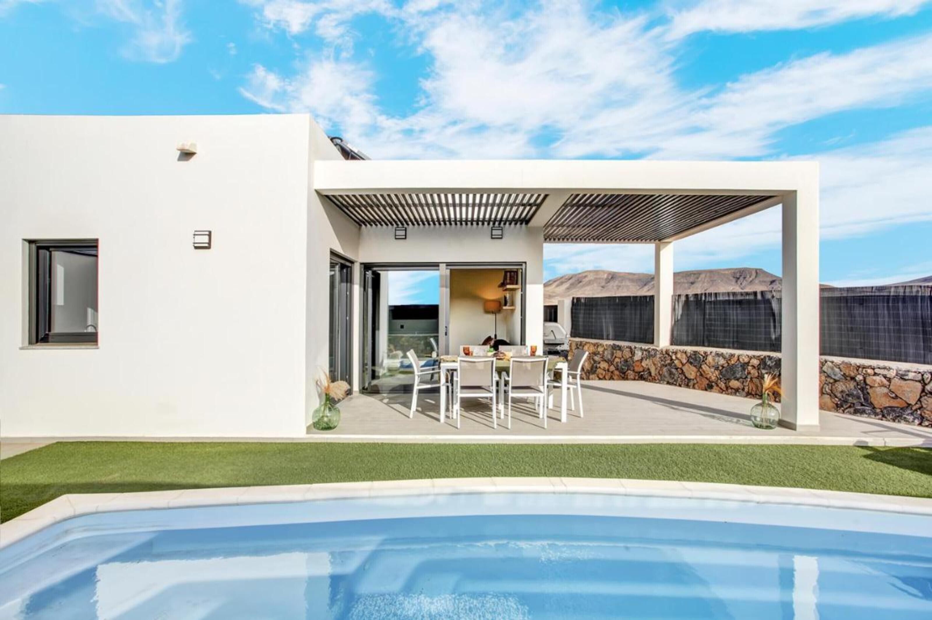 A modern house with a pool, patio, and a view of the mountains.