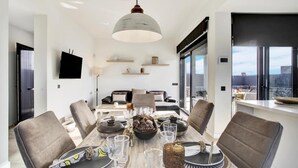 Een moderne eetruimte met een grote tafel, stoelen en een hanglamp.