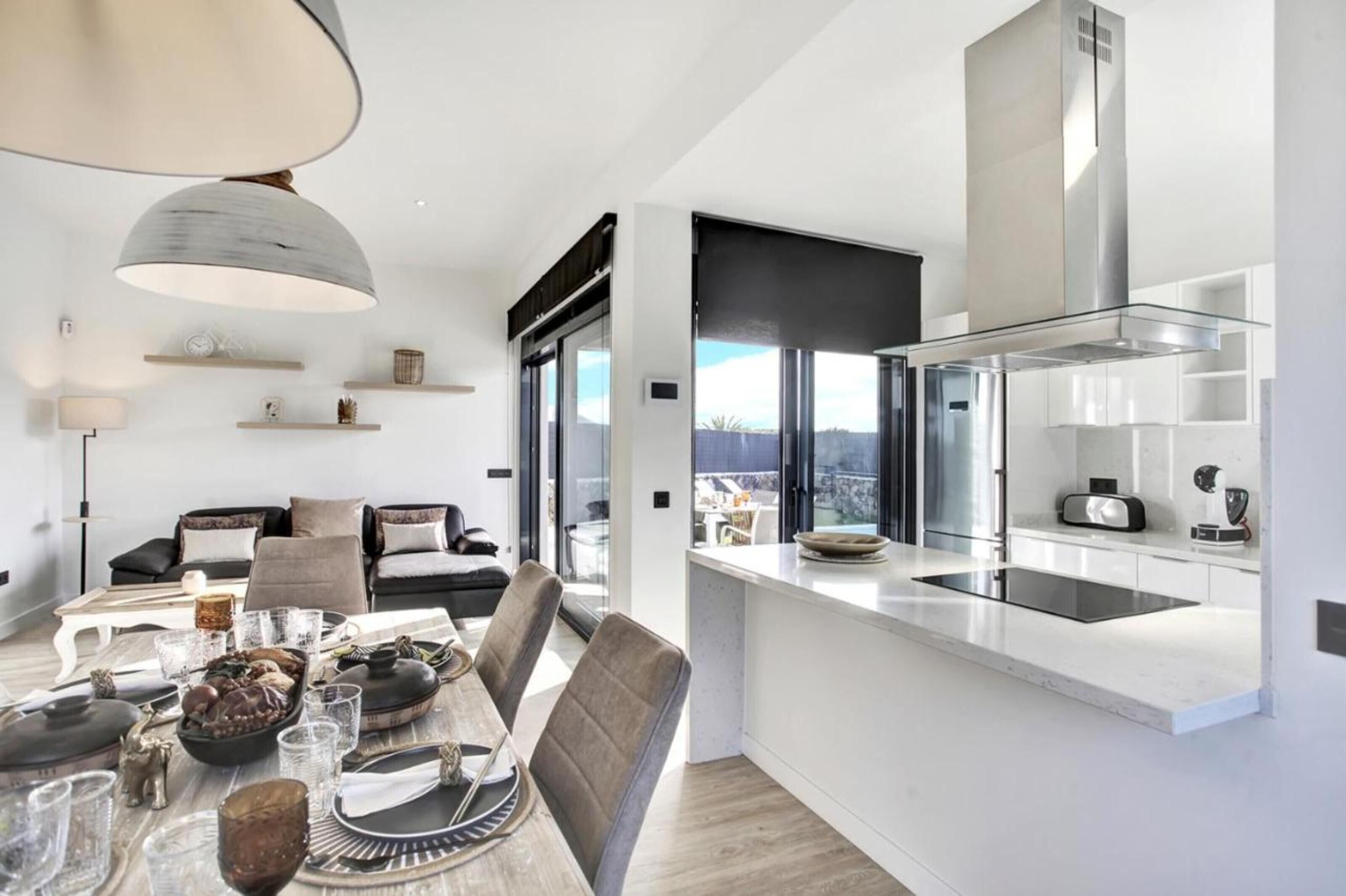 A modern kitchen with a built-in stove, a dining area with a table set for a meal, and a living area with a sofa and a lamp.