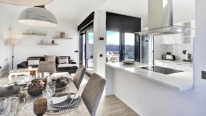 Een moderne keuken met een ingebouwde kookplaat, een eethoek met een tafel gedekt voor een maaltijd, en een zithoek met een bank en een lamp.