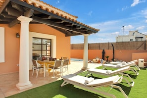A patio with a pool, lounge chairs, and a table with chairs.