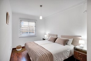 A bedroom with a bed, bedside tables, a lamp, a window with blinds, a woven basket, and a wooden floor. - Vacation Home 'Villa Corralejo' with Private Pool, Private Terrace and Wi-Fi (Geafond)