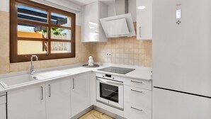 A modern kitchen with white cabinetry, a built-in oven, a sink, and a window with a view of palm trees.