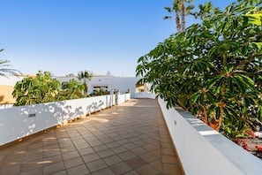 A rooftop terrace with a tiled floor, white walls, and green plants.